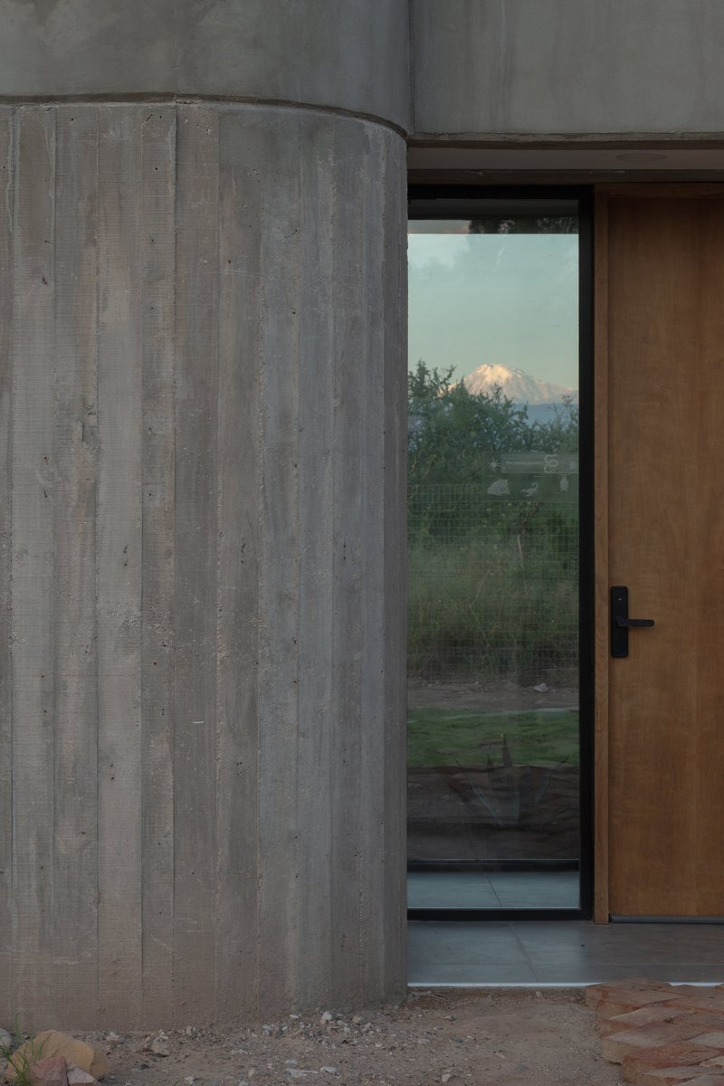 Curved concrete wall beside a timber door with a snow-capped mountain visible at dusk