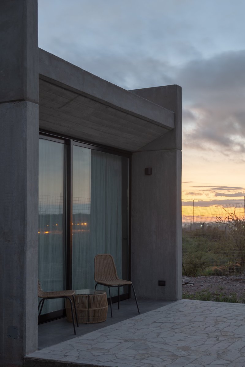 Covered terrace with concrete overhang and glass doors overlooking the landscape at sunset