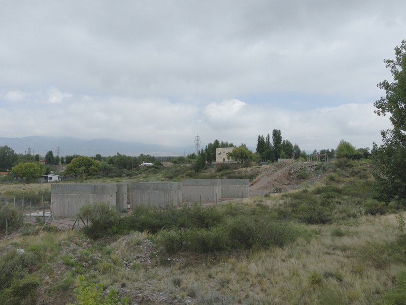 Board-formed concrete retaining wall set into a hillside with sparse vegetation and distant mountains