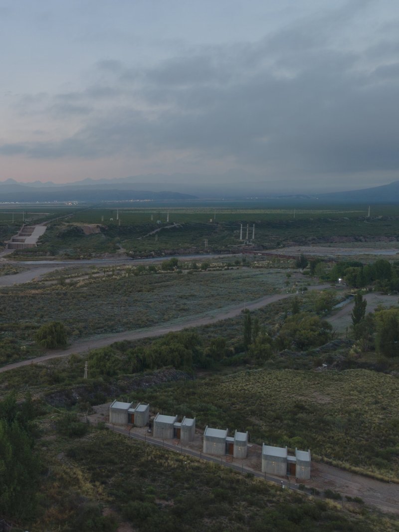 Aerial view of concrete volumes aligned in scrubland at dusk with distant fields and mountains