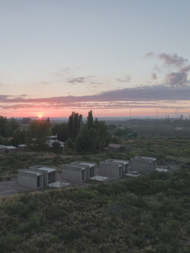 Cluster of concrete volumes with dark window openings in scrubland at sunrise