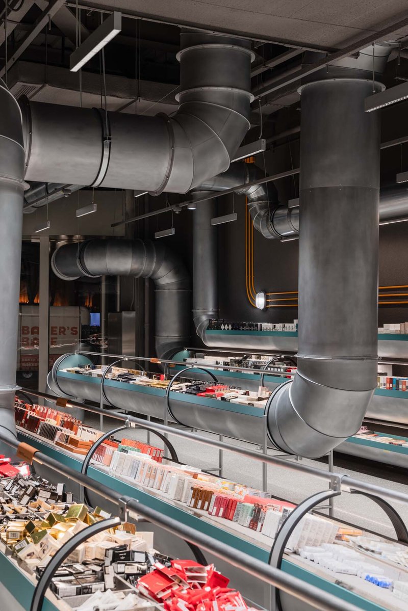 The image showcases an industrial-style retail space with prominent exposed ductwork integrated into the design. Metal pipes run throughout the ceiling and are