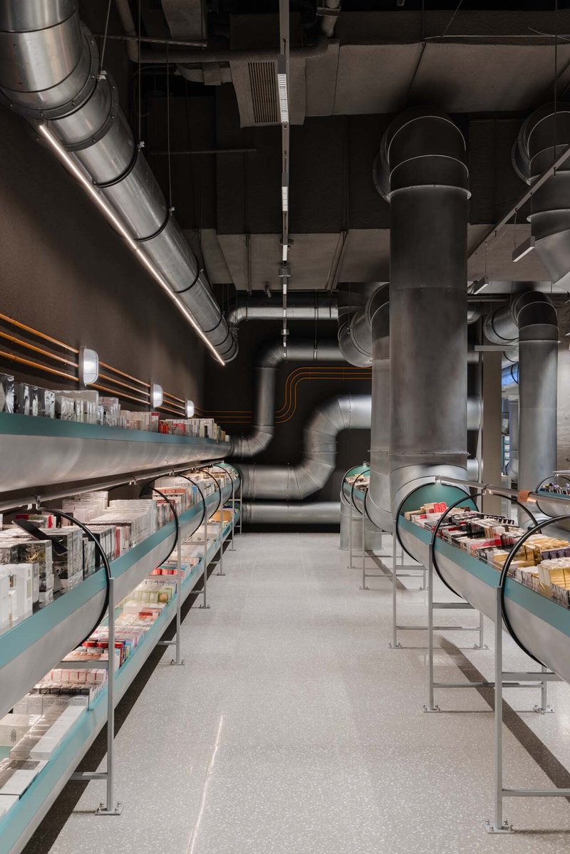 Retail interior with exposed metal ductwork threading between turquoise display shelves and cylindrical columns