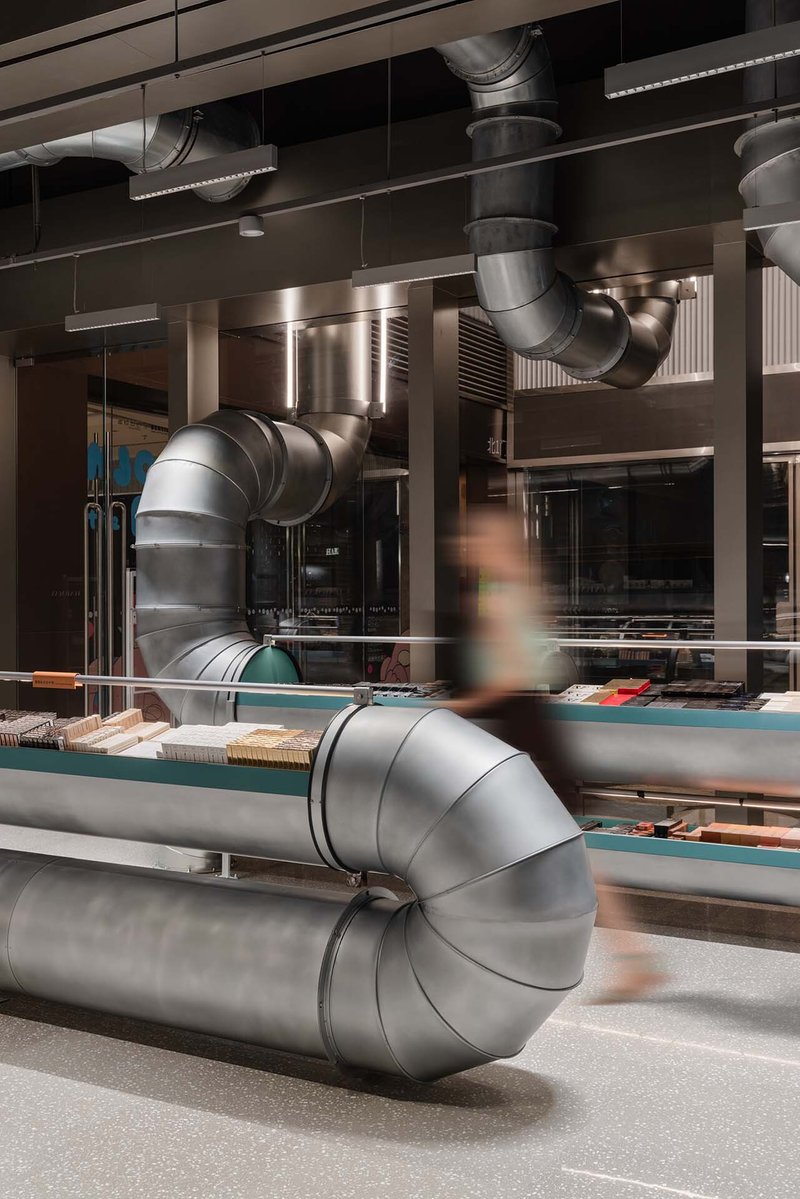 Curving metal ventilation duct crossing the retail floor as a blurred figure passes behind