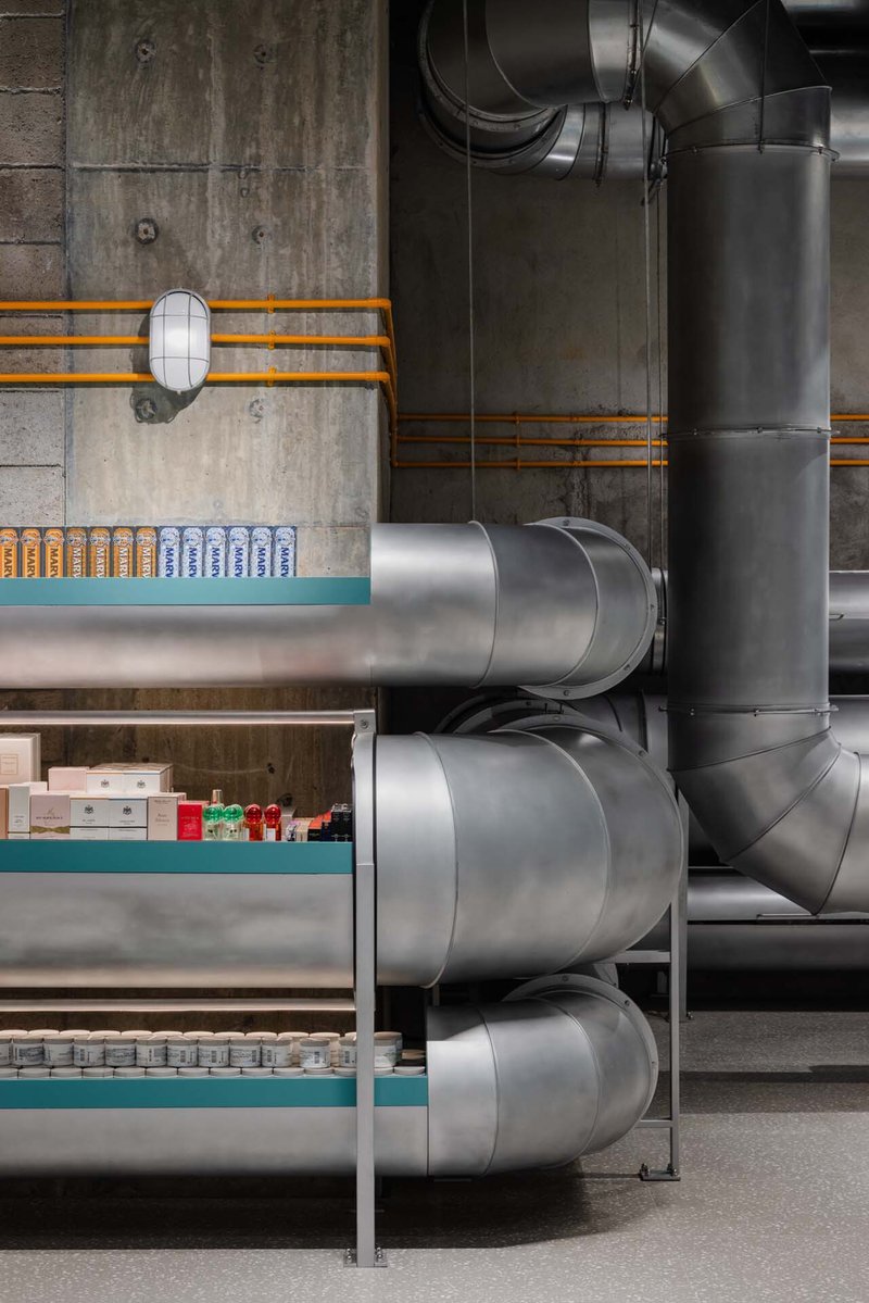 Stacked horizontal ducts emerging from concrete wall beside retail shelving with orange electrical conduit