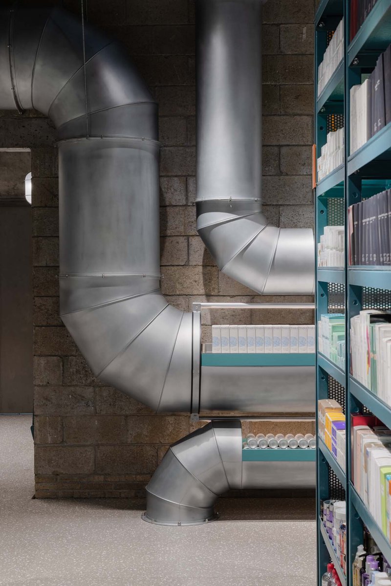 Exposed galvanized steel ductwork snaking through a stone block interior with teal shelving units