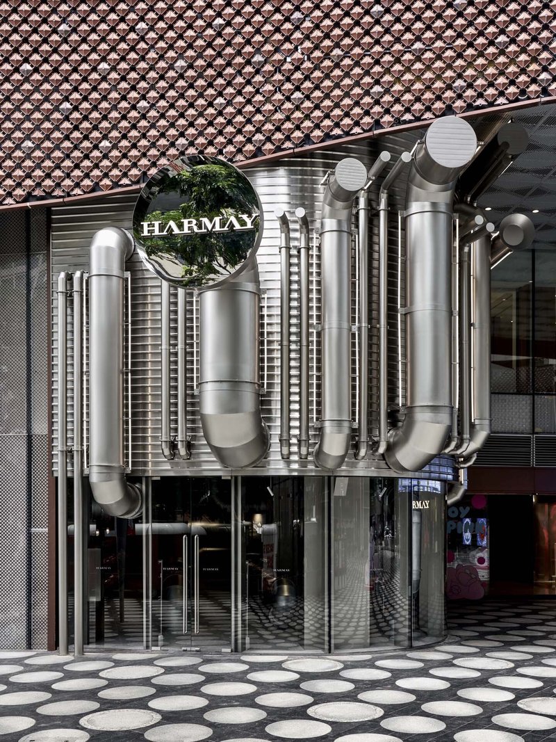 Facade entrance with polished stainless steel ductwork beneath a tiled canopy and circular floor pattern