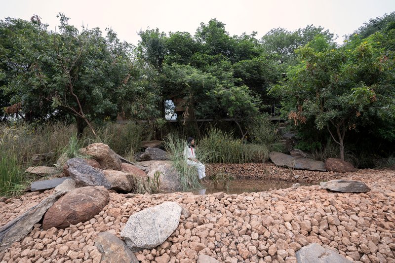 Natural pond surrounded by boulders and pebble beach with a figure wading in shallow water