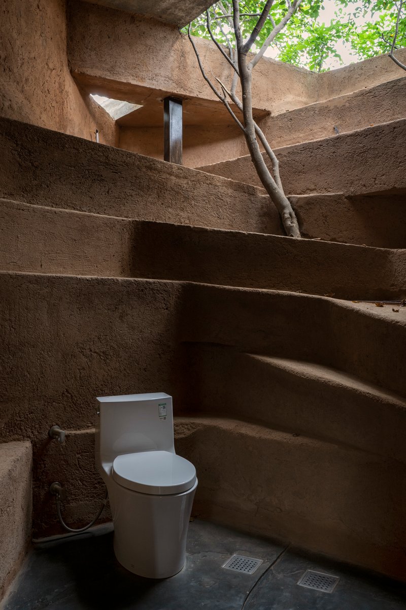 Bathroom with terraced earthen walls and skylight opening revealing tree branches above
