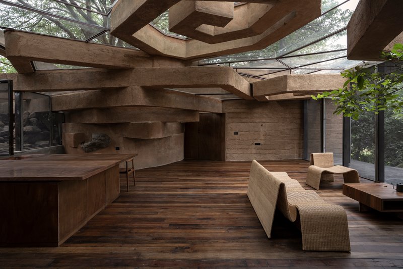 Interior showing the sculptural rammed earth ceiling planes above timber floors and woven furniture