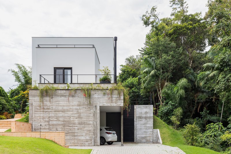 Board-formed concrete retaining wall base with upper white volume and rooftop terrace surrounded by dense forest
