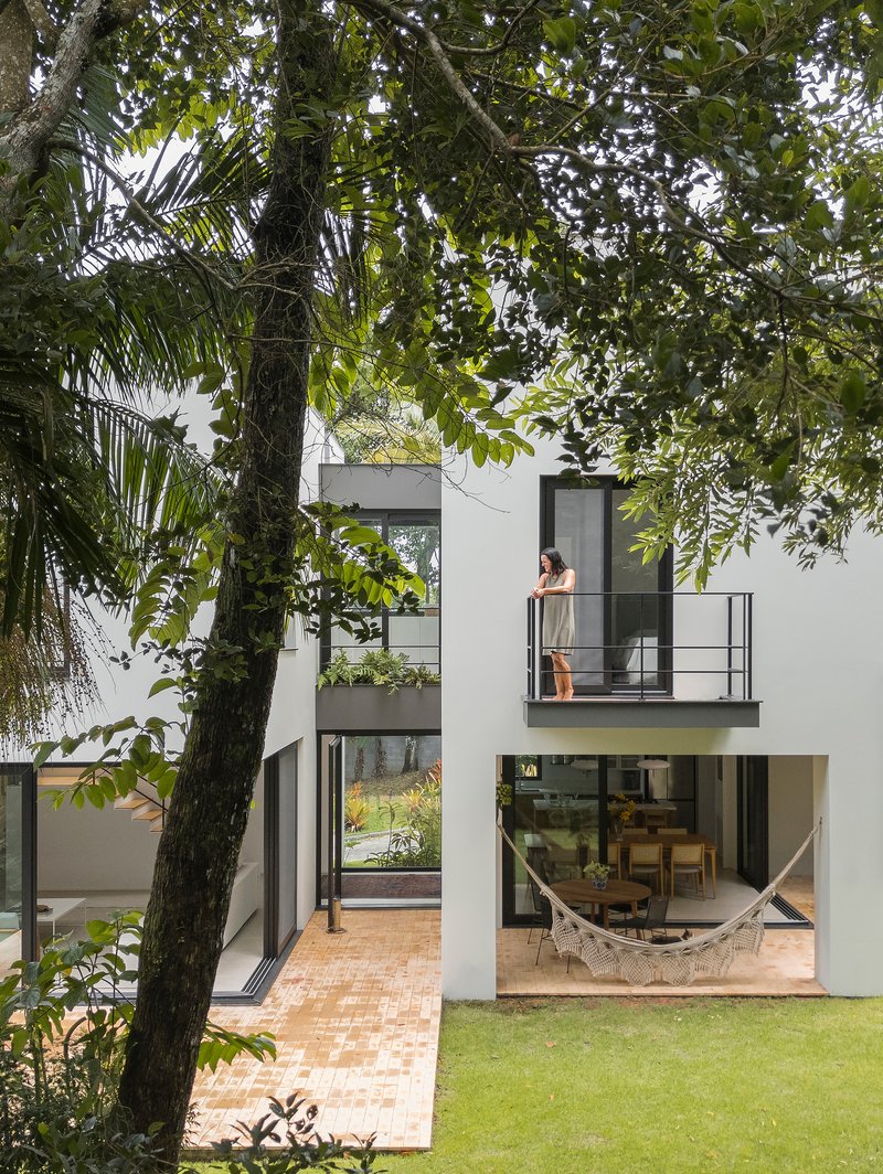 Cantilevered balcony with steel railing and figure seen through trees next to glazed living space