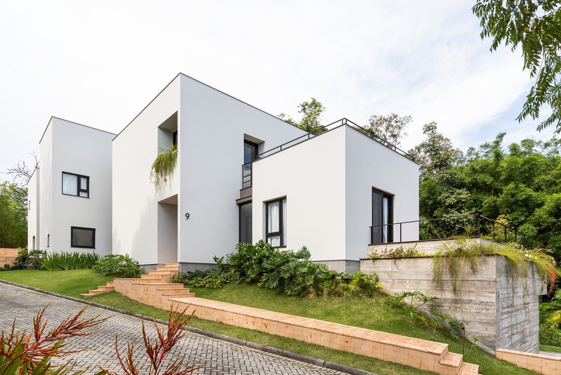 Street view of white stucco volumes on terraced lawn with timber-edged steps and concrete retaining wall