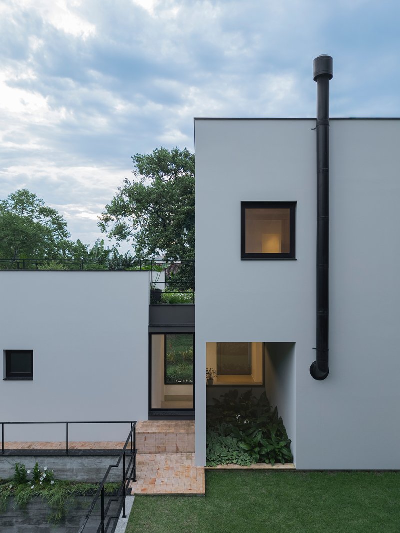 External black metal chimney flue rising along the white facade above recessed glazed entry