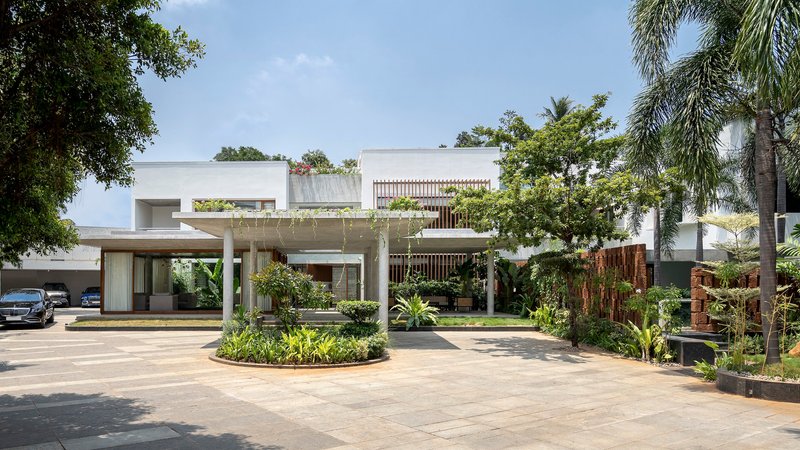 Entry driveway view showing white concrete canopy, timber screens, and circular planted island