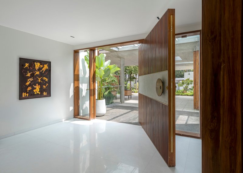 Entry foyer with pivoting timber door opening to concrete columns and greenery beyond