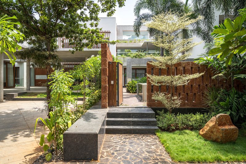 Garden courtyard with textured red stone wall, concrete steps, and planted beds beneath palm trees