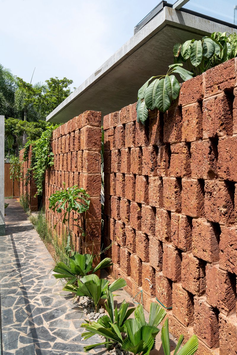 Perforated red volcanic block wall with concrete canopy above and tropical planting along the paved walkway