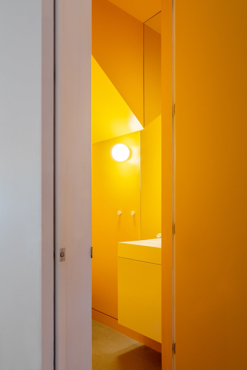 View through a narrow doorway into a fully tiled bathroom with yellow surfaces and circular wall sconce