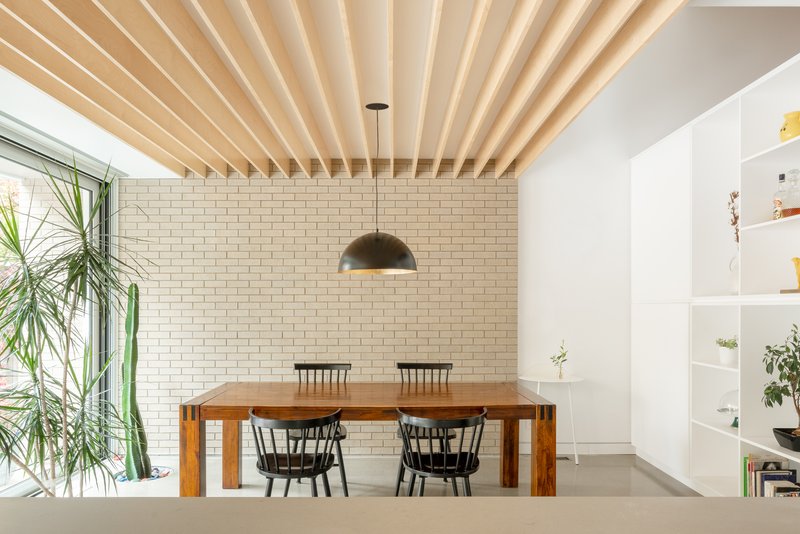 Dining room with exposed timber beam ceiling and cream brick wall beside a window with plants
