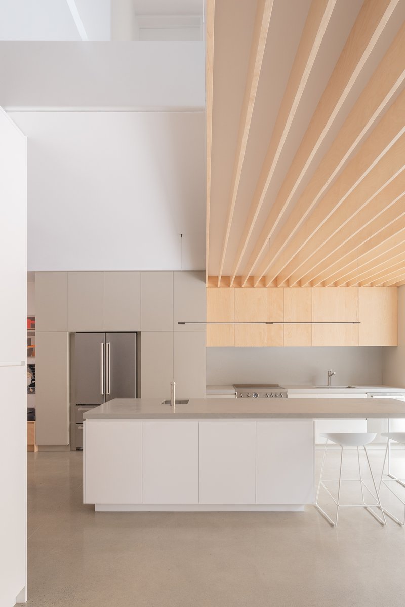 Kitchen with white island and ribbed timber ceiling transitioning into white painted volume