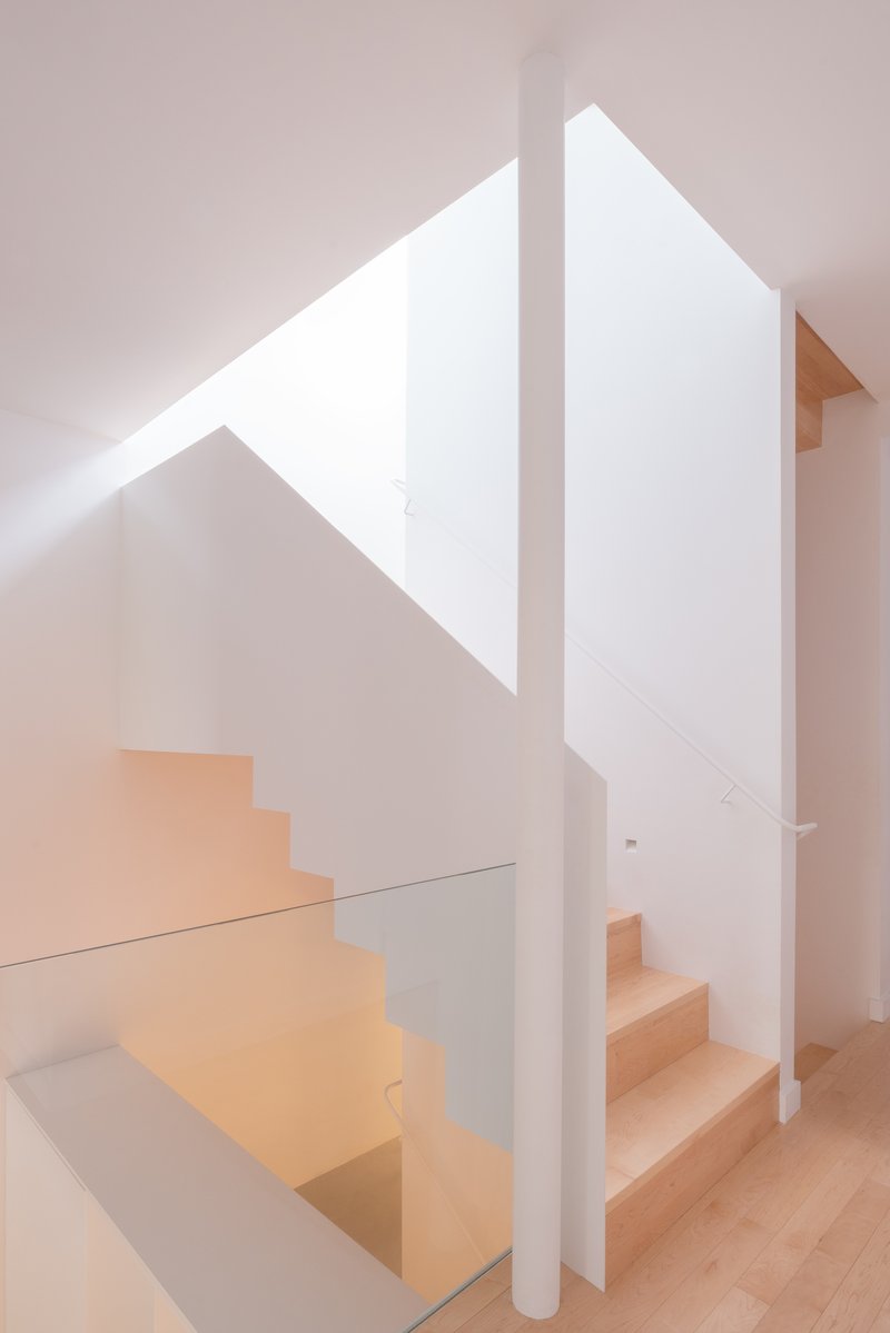 Light timber staircase wrapping around a white column beneath a triangular skylight
