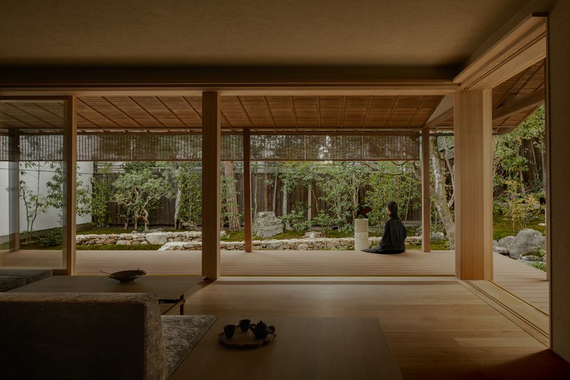 Timber-framed pavilion opening onto a rock garden with moss, stones, and a seated Buddha sculpture