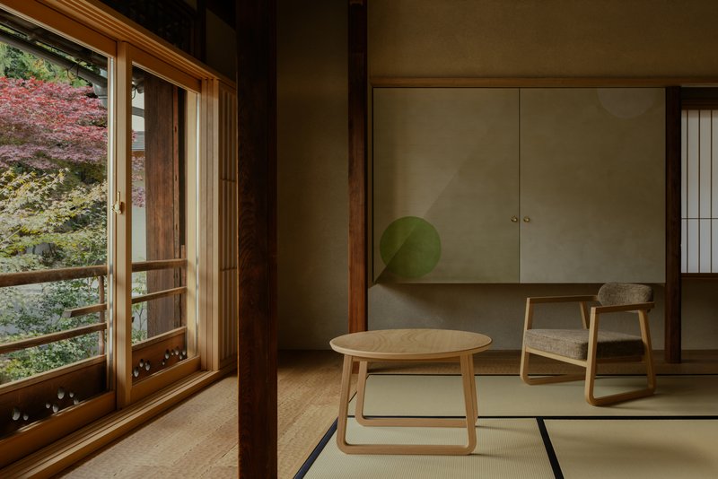 Tatami room with low table, chair, and sliding doors opening to autumn foliage