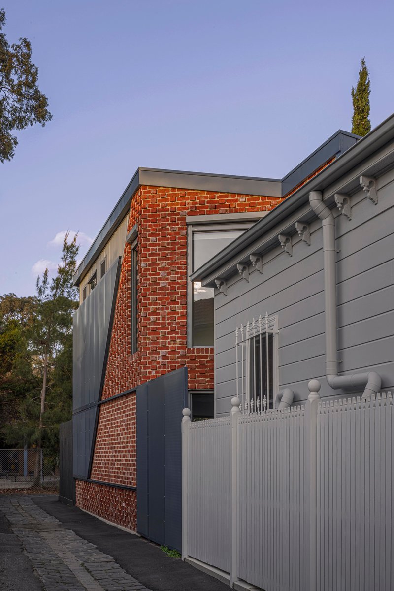 Street view of the brick and weatherboard facade with white picket fence at dusk