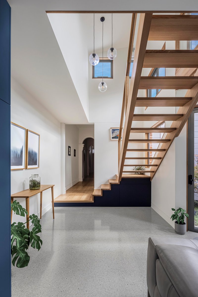 Entry hall with timber open-tread staircase and pendant globe lights beside potted plants