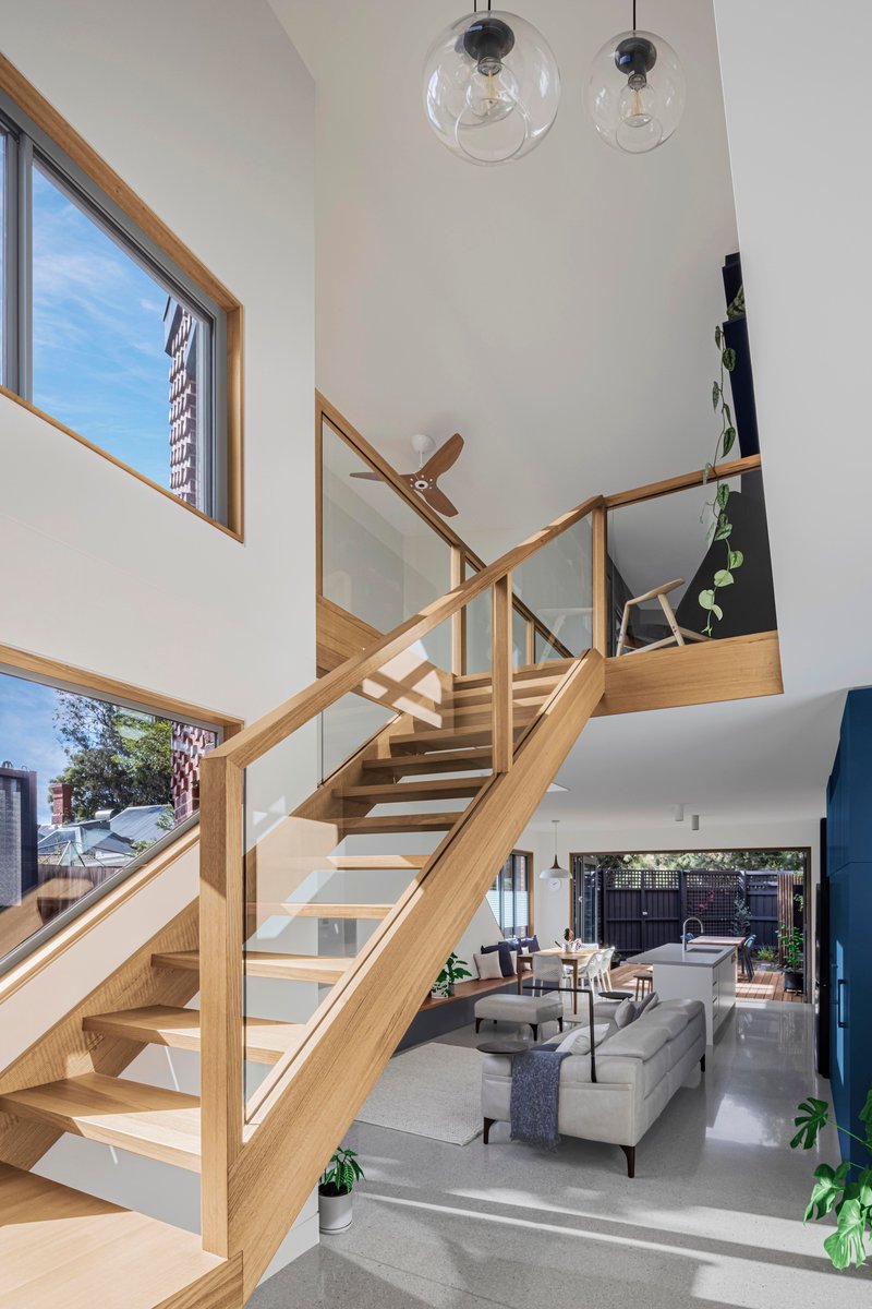 Double-height living space with timber and glass staircase overlooking the open-plan interior