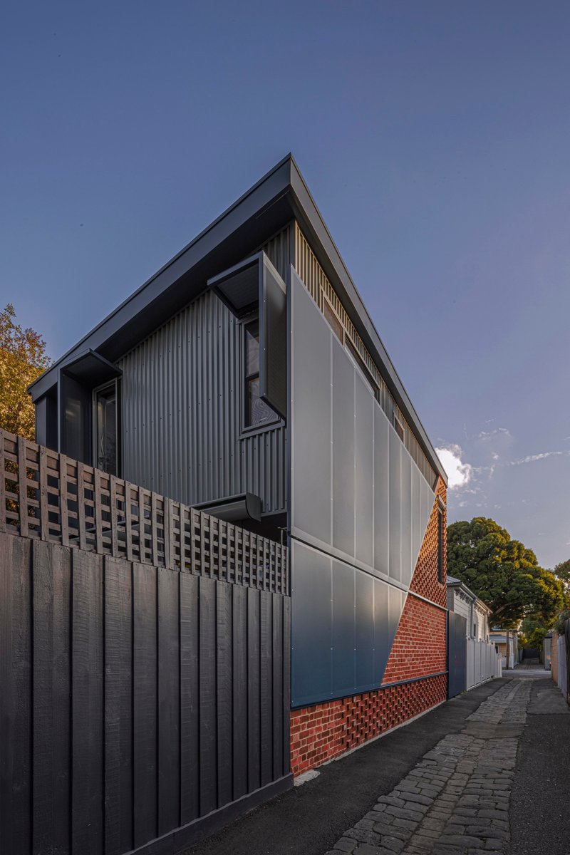 Laneway elevation showing the corrugated metal upper level and patterned brick base at dusk