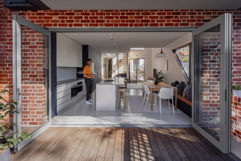 Open-plan kitchen and dining room framed by folding glass doors and red brick courtyard walls