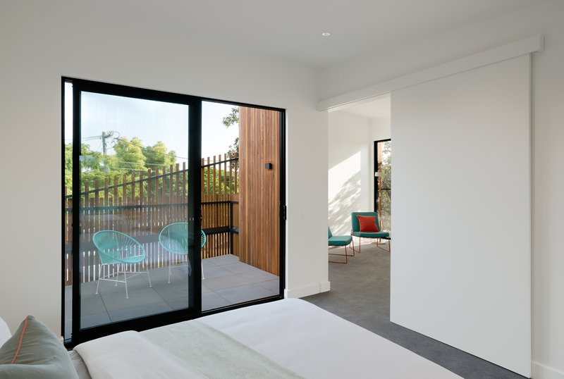 Bedroom with black-framed glass doors opening to a terrace with timber screening and turquoise chairs