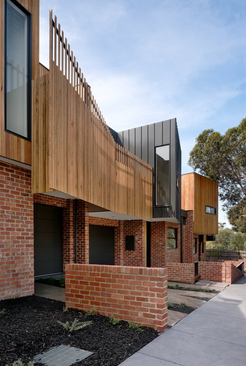 Entry sequence with red brick wall, vertical timber screen and planted bed along concrete path