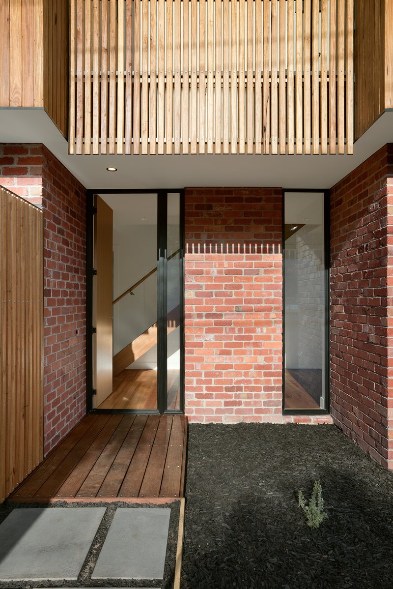 Courtyard view showing timber slatted screen overhead and brick walls flanking glazed entry doors