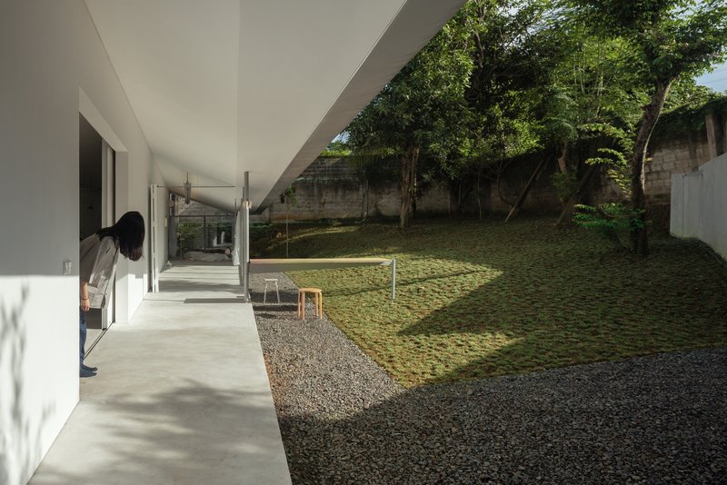 Covered walkway with white soffit opening to a sunlit courtyard with gravel paths and grassed embankment