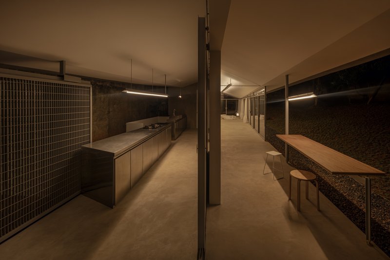Linear kitchen with timber cabinetry and mesh sliding doors opening to gravel courtyard