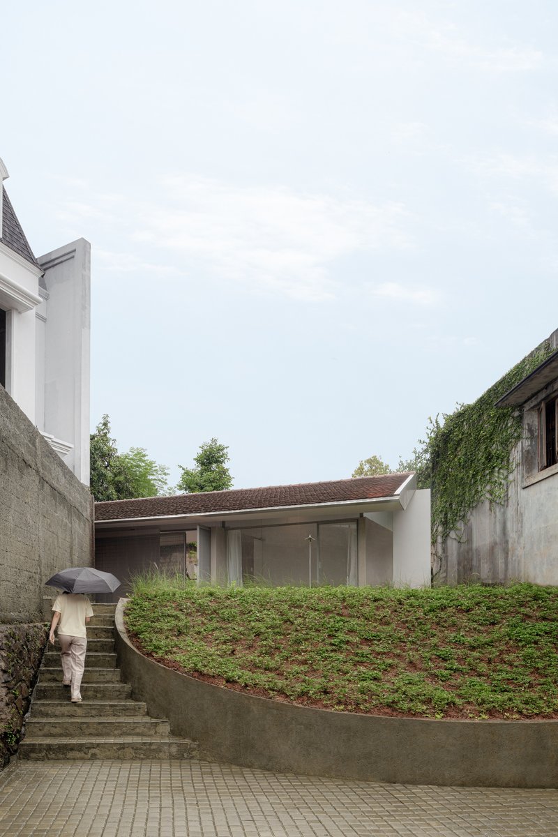 Person with umbrella ascending concrete steps beside the planted green roof under overcast sky