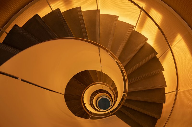 Top-down view of a spiral staircase with timber treads and metal handrail under warm lighting