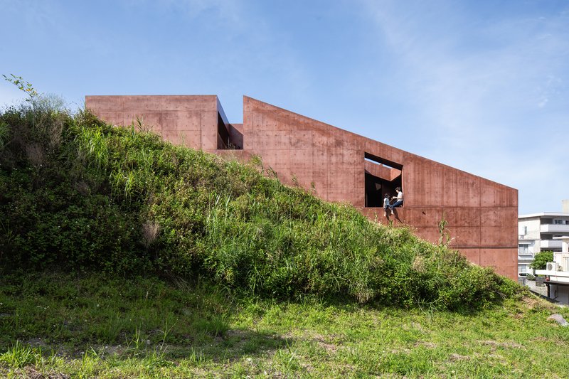 Rammed earth volumes embedded in a grassy hillside with a figure visible in an upper opening