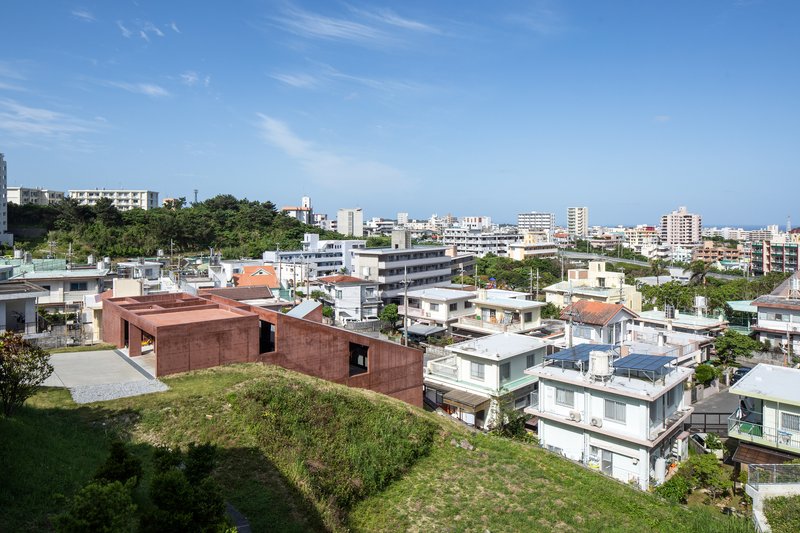 Aerial view of rammed earth volumes set among low-rise residential buildings on a sloped site