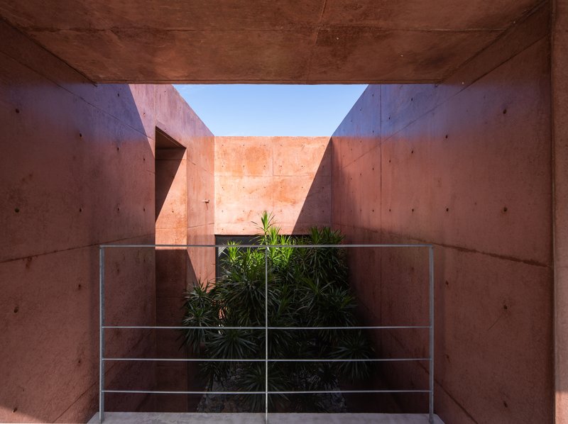 Interior courtyard framed by rammed earth walls with a glass-paneled guardrail overlooking planted beds below