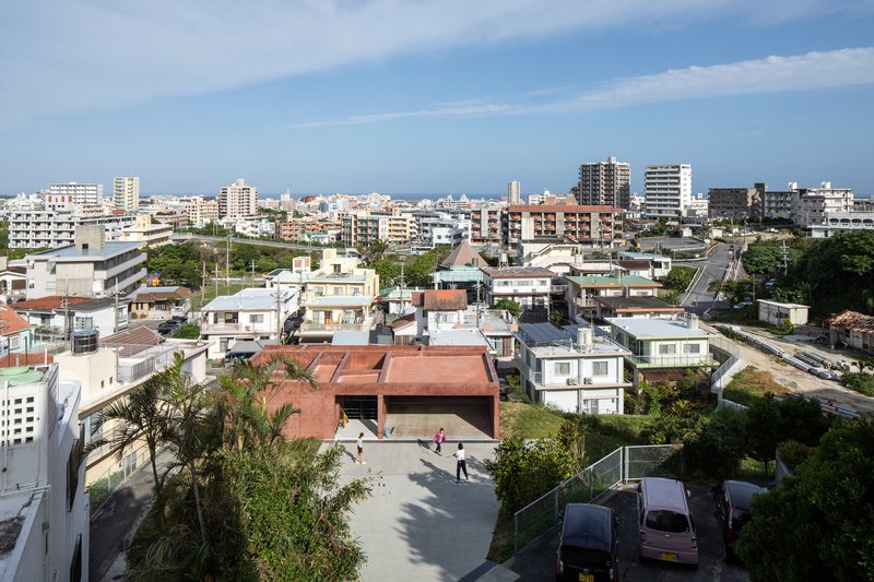 Elevated view of the rammed earth roof among neighborhood houses and apartment blocks under bright sky