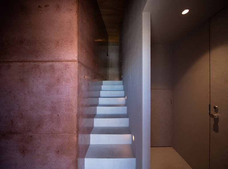 Concrete staircase rising between exposed aggregate walls and white plaster surfaces under recessed lighting