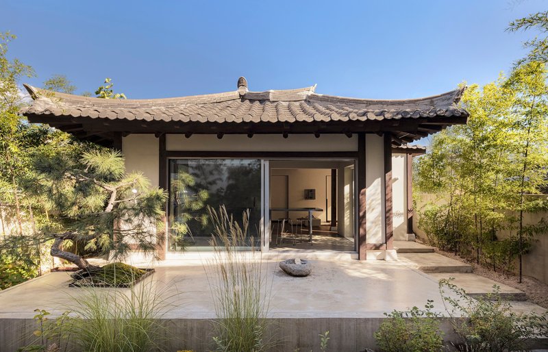 Pavilion with curved tile roof and timber columns opening onto a terrace with pine and bamboo