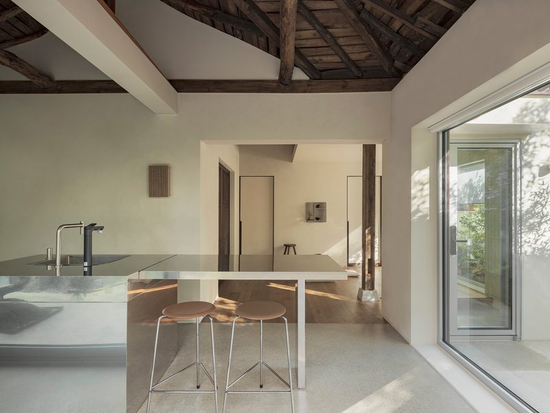 Kitchen island with bar seating beneath exposed timber roof trusses and afternoon sunlight