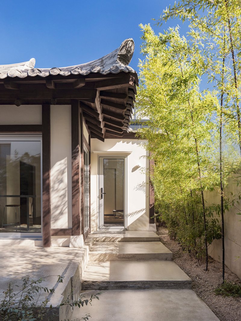 Entry sequence with timber columns and tiled eaves beside tall bamboo in clear daylight