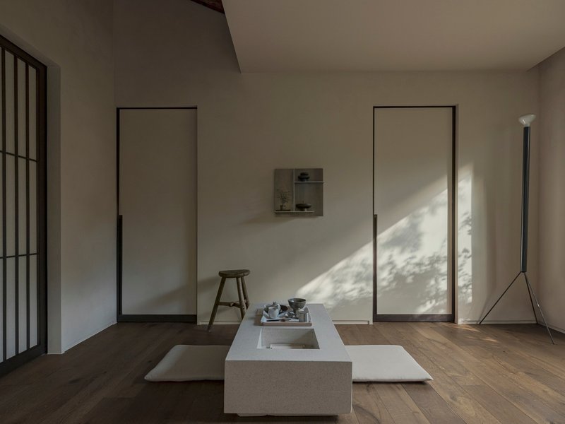 Minimalist interior with flush panel doors, low stone platform and dappled sunlight across oak floors