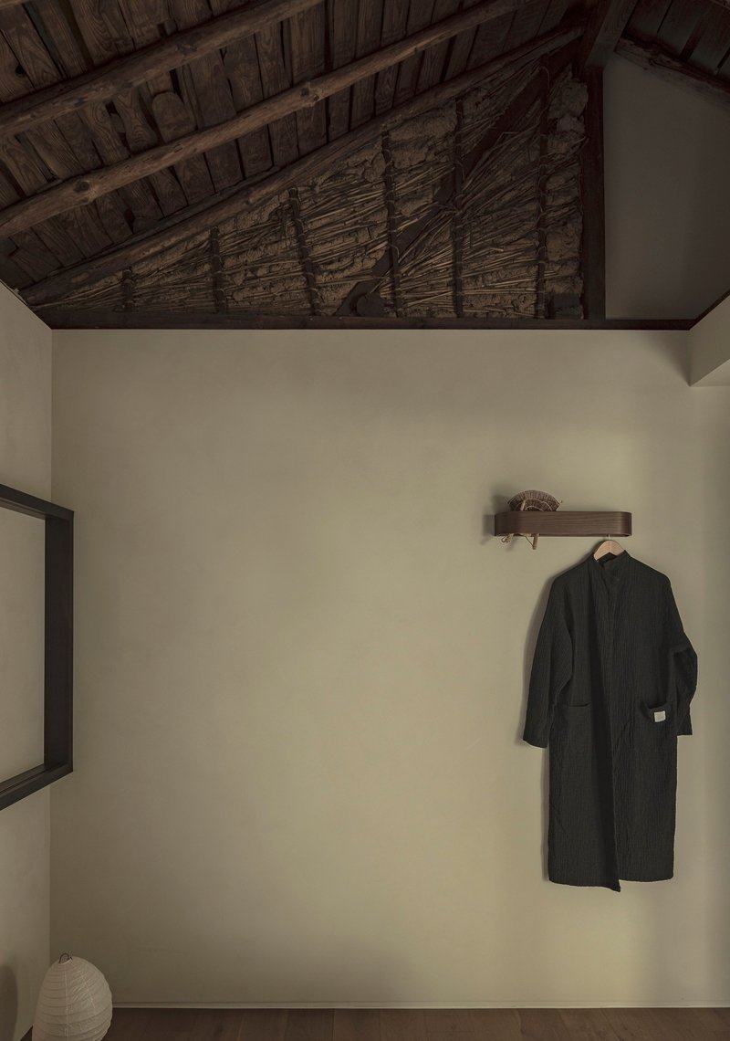 White plastered wall below exposed timber ceiling beams with a hanging coat and paper lantern